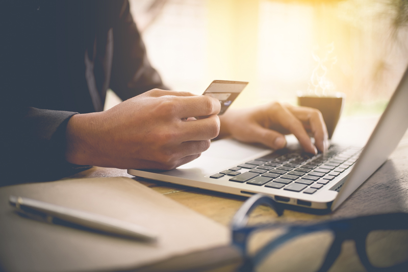 Hand holding credit card while typing on a laptop